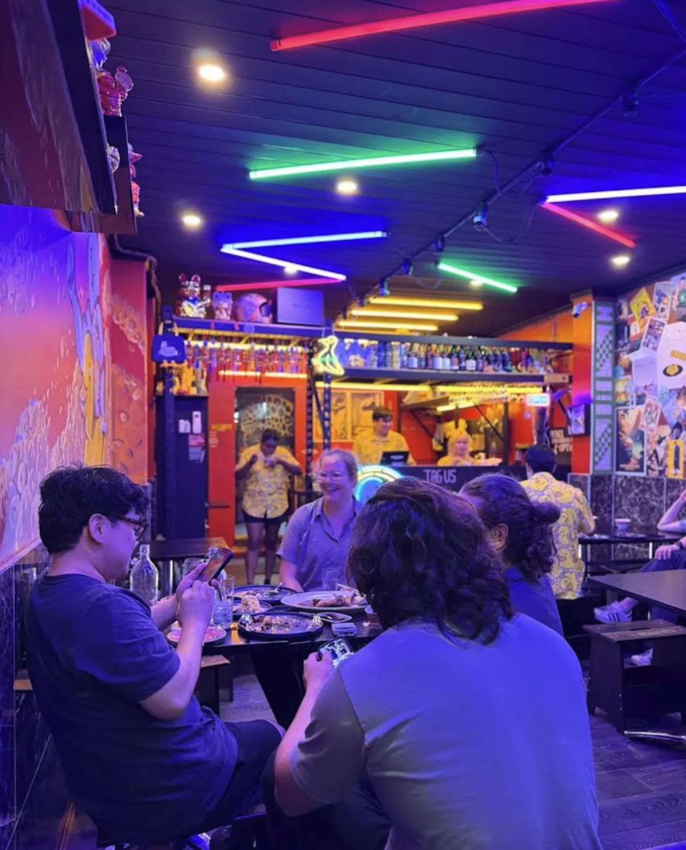 Diners at a table in a small restaurant lit by colourful neon tubes.